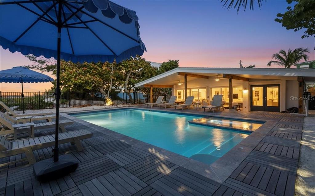 A swimming pool with a spa sits on a wooden deck beside a modern house — 102 TUNA STREET, ANNA MARIA, FL