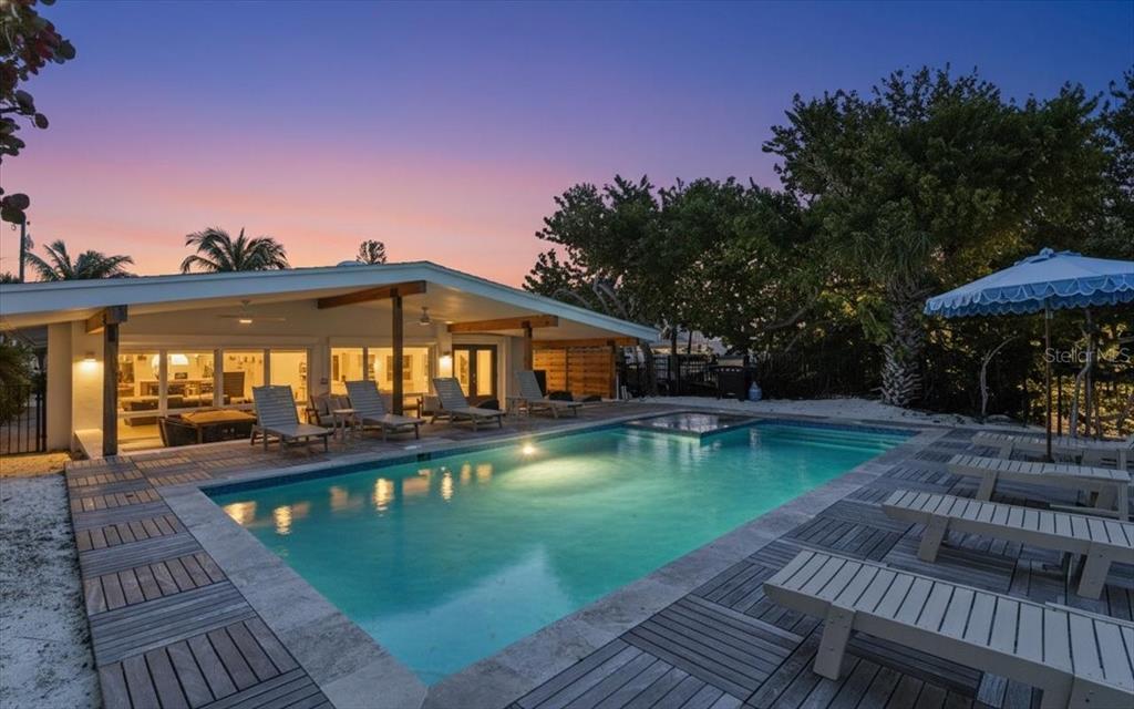 A swimming pool with a wooden deck sits in front of a house at sunset — 102 TUNA STREET, ANNA MARIA, FL