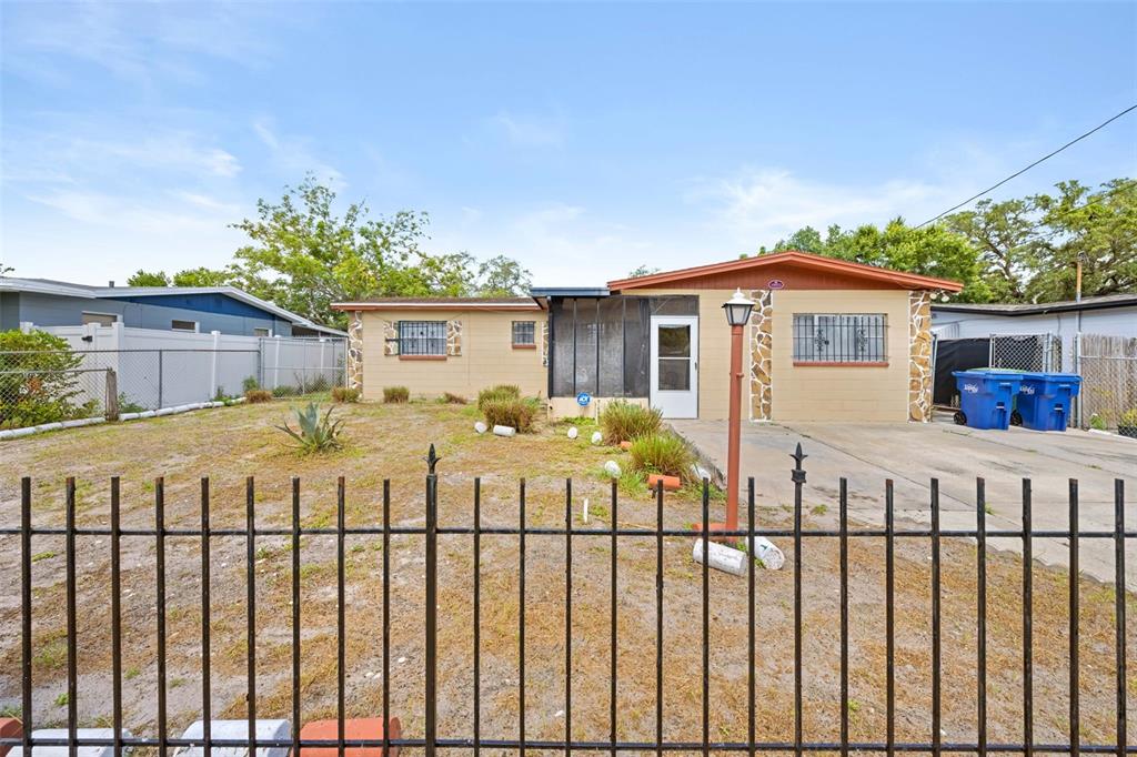 A single-story house with a tan exterior, screened porch, and metal fence in the yard — 10412 N ALTMAN STREET, TAMPA, FL