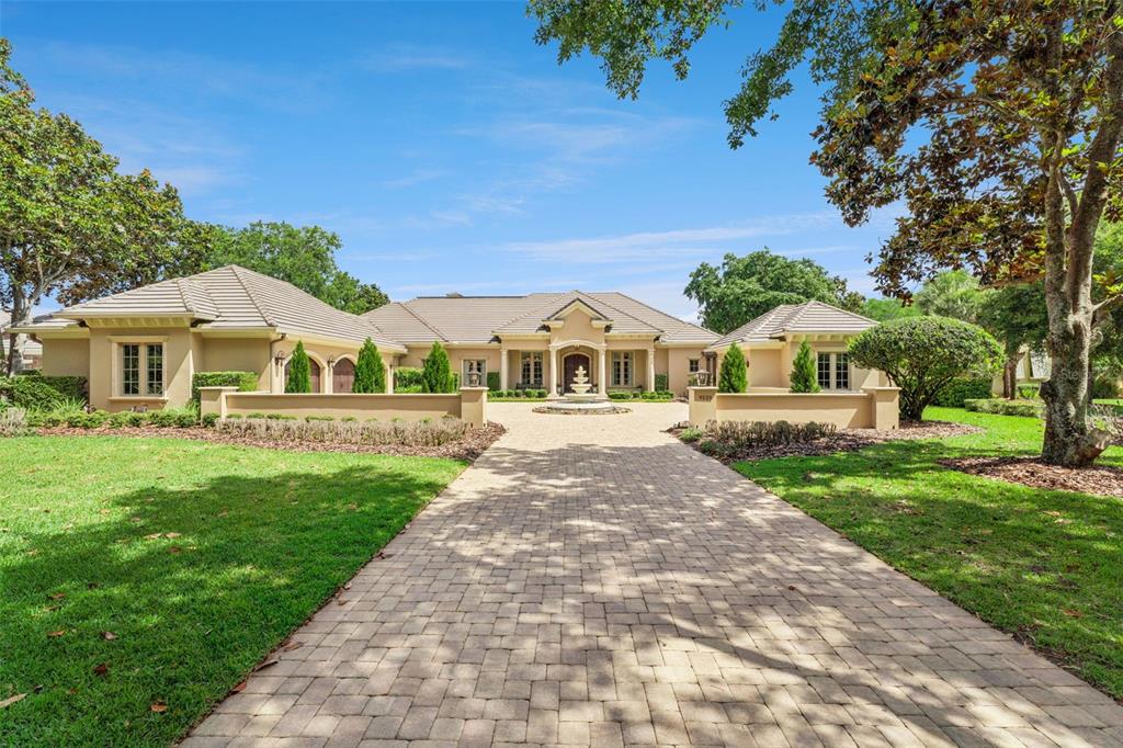 A large, single-story beige house with a paved driveway and a central fountain — 9225 BEVINGTON LANE, ORLANDO, FL