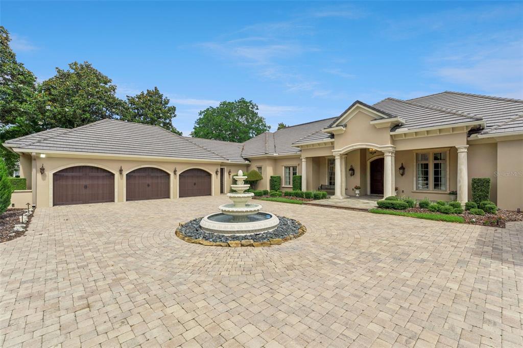 A beige house with a three-car garage and a tiered fountain in the circular driveway — 9225 BEVINGTON LANE, ORLANDO, FL