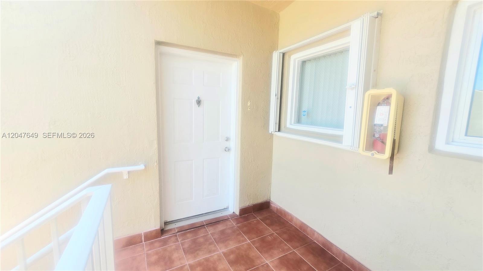 A white door and a window with a fire extinguisher are on a tiled balcony — 15771 SW 137th Ave # 203, Miami FL 33177, MIAMI, FL