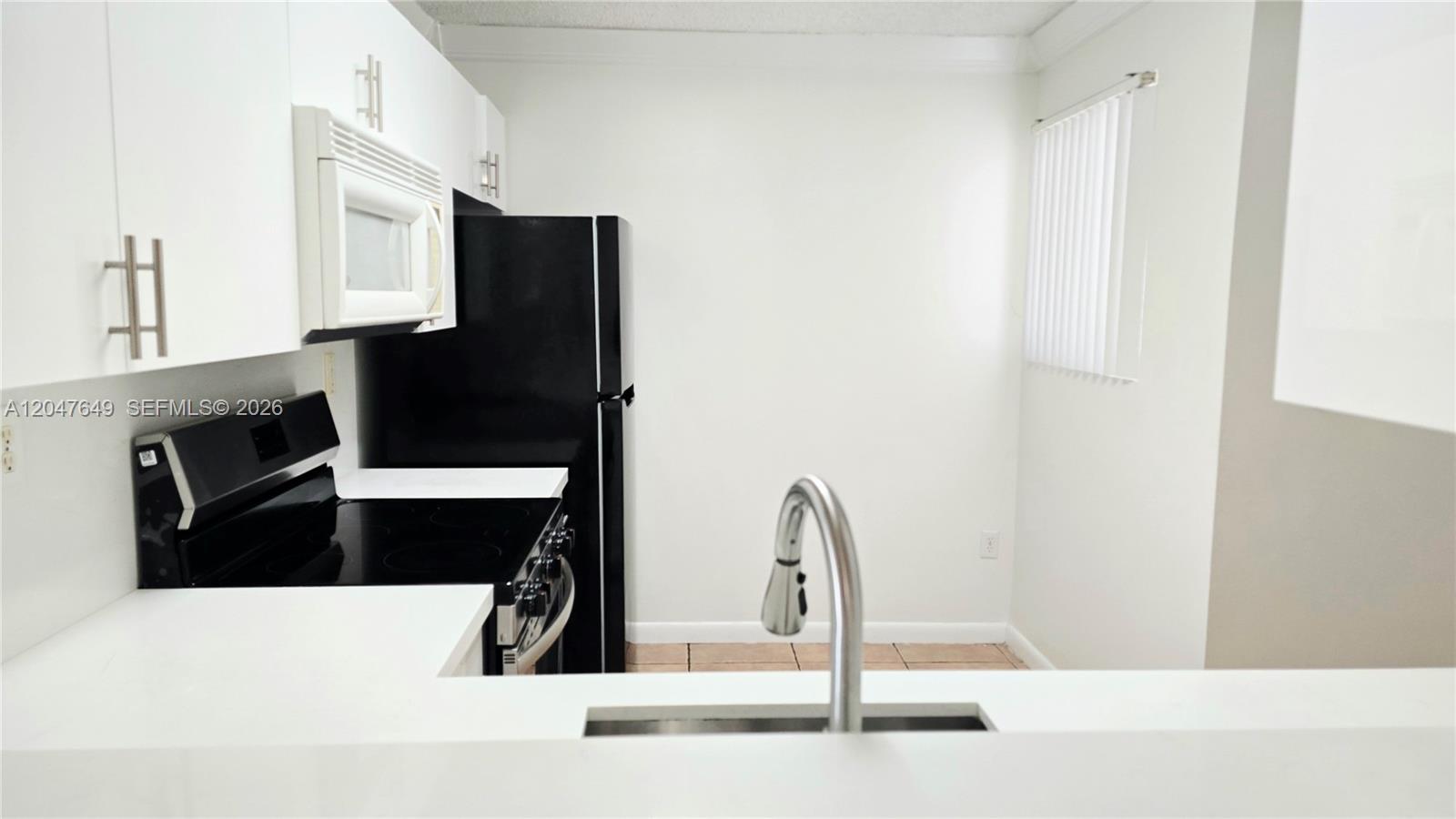 A kitchen features white cabinets, black appliances, a stainless steel faucet, and tile flooring — 15771 SW 137th Ave # 203, Miami FL 33177, MIAMI, FL