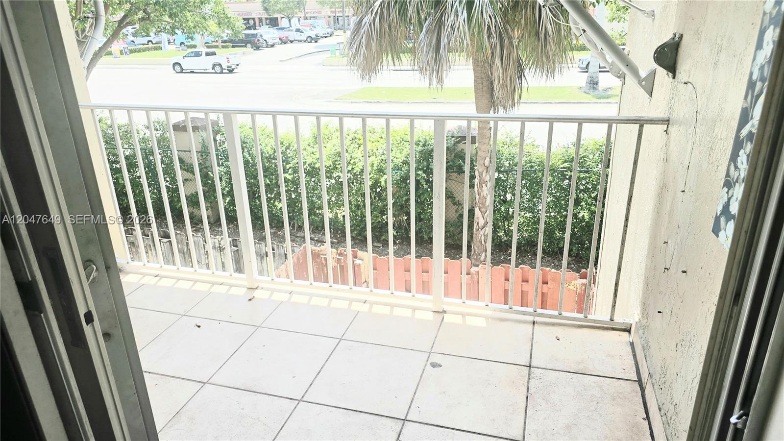 A balcony with light-colored floor tiles overlooks a street, a palm tree, and a fence — 15771 SW 137th Ave # 203, Miami FL 33177, MIAMI, FL