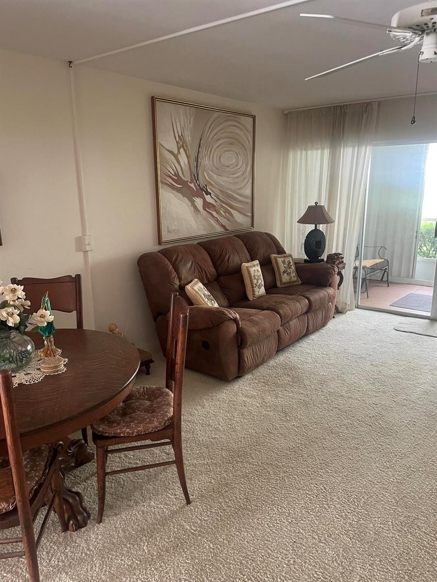 A living and dining area features a brown reclining sofa, round wooden table, and balcony access — 2 Garden Street # 106m, Tequesta FL 33469, TEQUESTA, FL