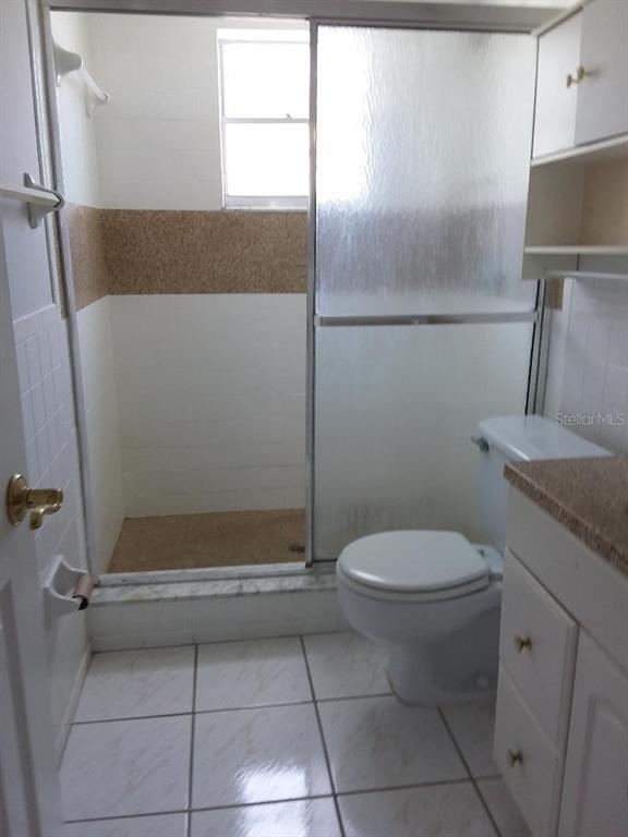 A bathroom features a tiled shower stall with sliding glass doors, a toilet, and white cabinetry — 4836 ONYX LANE, NEW PORT RICHEY, FL