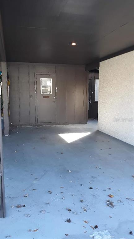 A covered concrete carport leads to a brown door with a window on a building exterior — 4836 ONYX LANE, NEW PORT RICHEY, FL