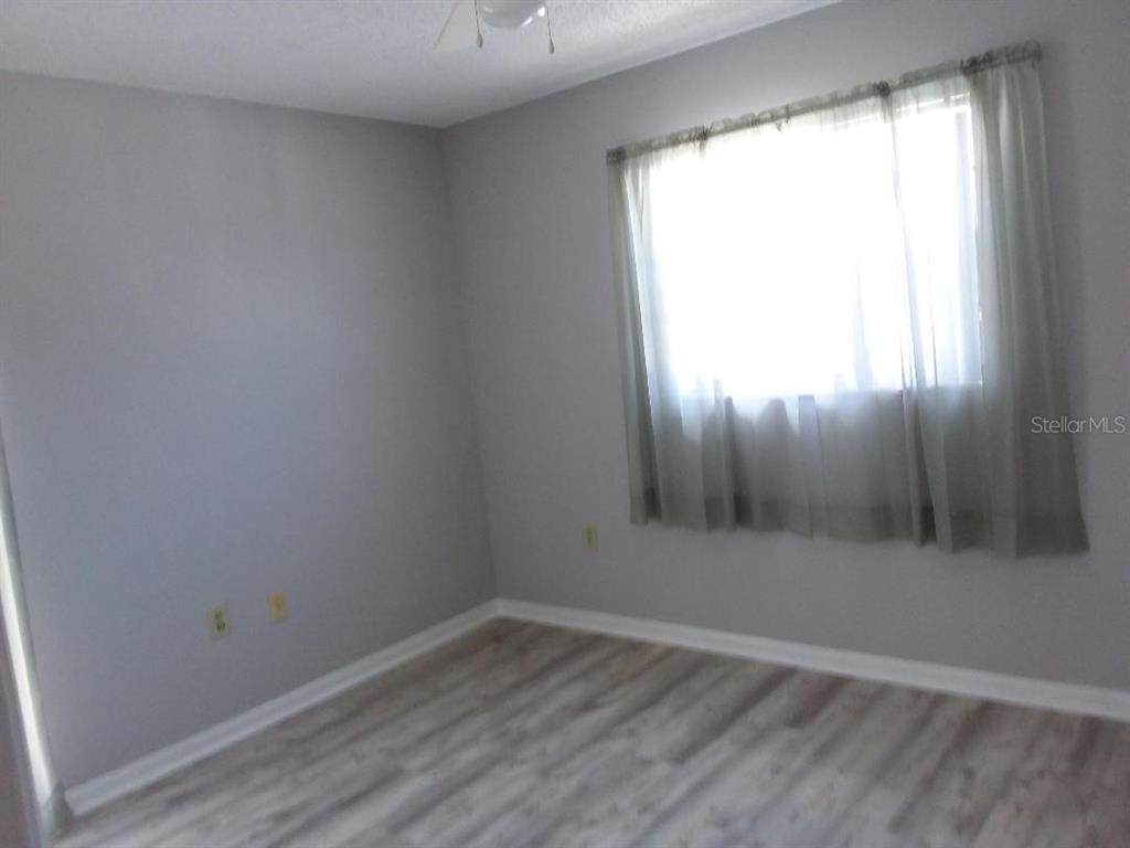 An empty bedroom features light gray walls, wood-look flooring, and a window with sheer curtains — 4836 ONYX LANE, NEW PORT RICHEY, FL