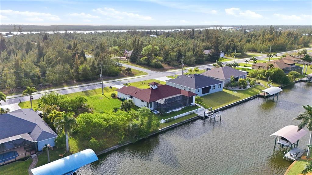 An aerial view shows a waterfront house with a red roof and pool cage — 9413 ST PAUL DRIVE, PORT CHARLOTTE, FL