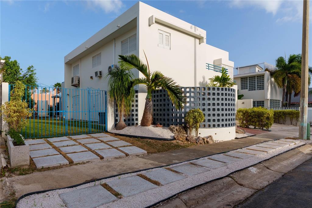 A white two-story house with a blue metal gate, palm trees, and a decorative block wall — 75 FRAGATA UNIT 75, GUANICA, PR