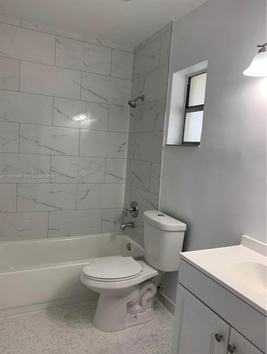 A bathroom features a white vanity, a toilet, and a bathtub with marble-look wall tiles — 7505 SW 82nd St # 306, Miami FL 33143, MIAMI, FL