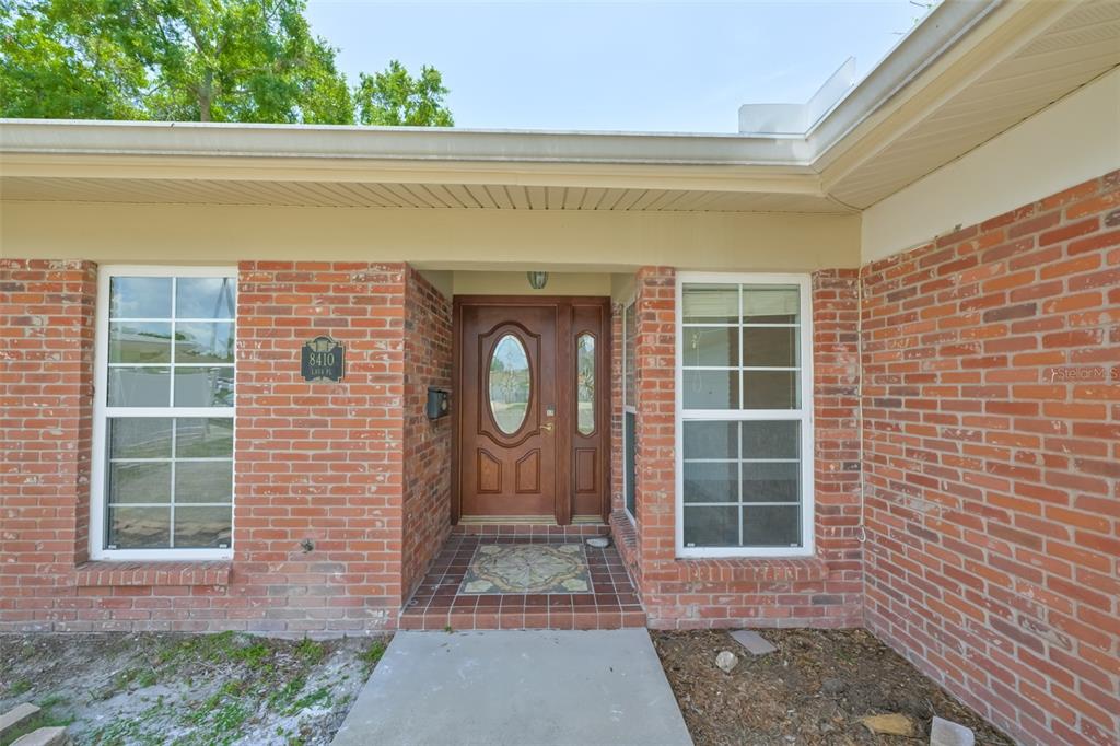 The front exterior of a brick house features a wooden door and two windows — 8410 LAVA PLACE, TAMPA, FL