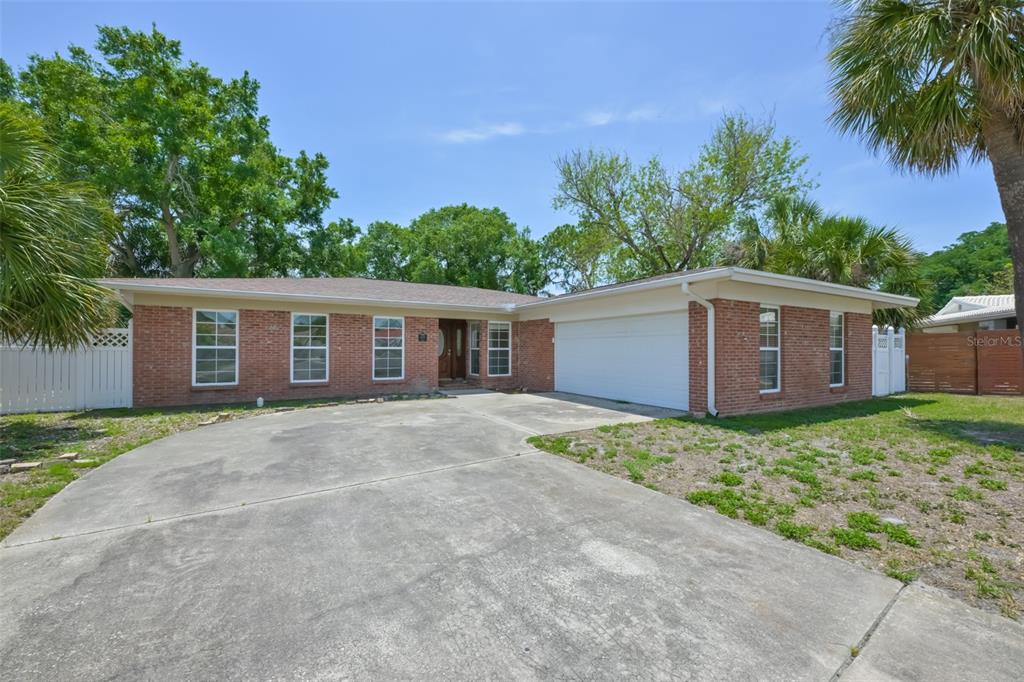 A single-story brick house features a concrete driveway, a two-car garage, and mature trees — 8410 LAVA PLACE, TAMPA, FL