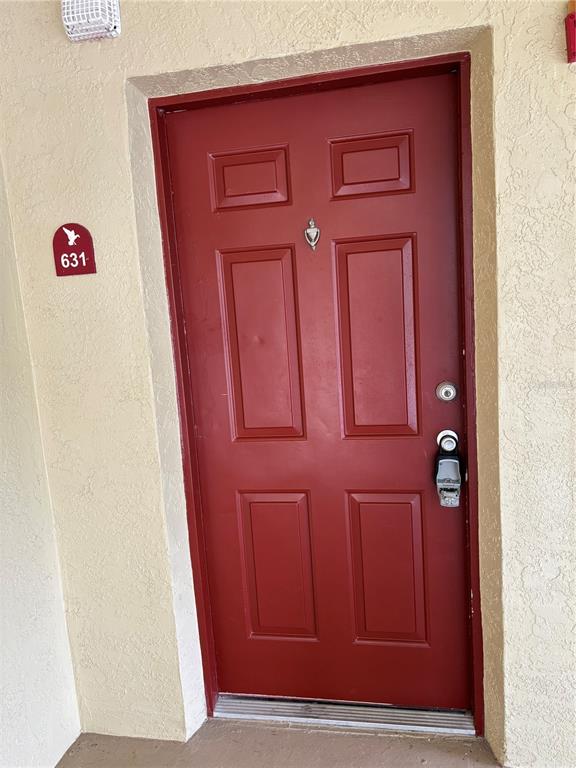 A red front door with a door knocker and a lockbox is set in a stucco wall — 2690 CORAL LANDINGS BOULEVARD UNIT 631, PALM HARBOR, FL