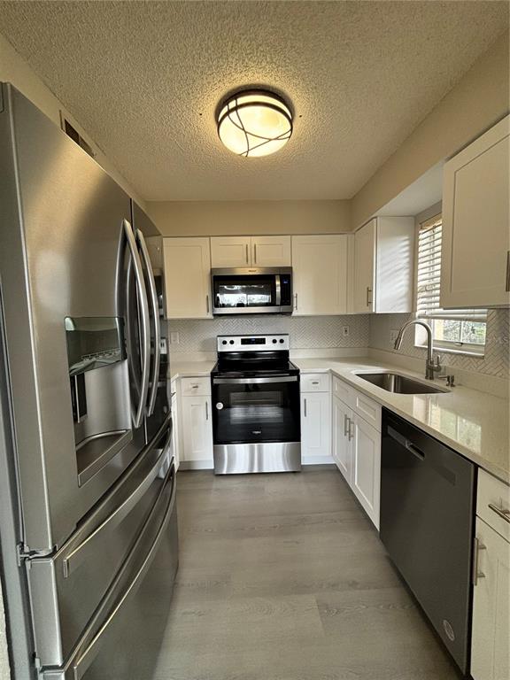 A galley kitchen features white cabinets, stainless steel appliances, light countertops, and wood-look flooring — 2690 CORAL LANDINGS BOULEVARD UNIT 631, PALM HARBOR, FL