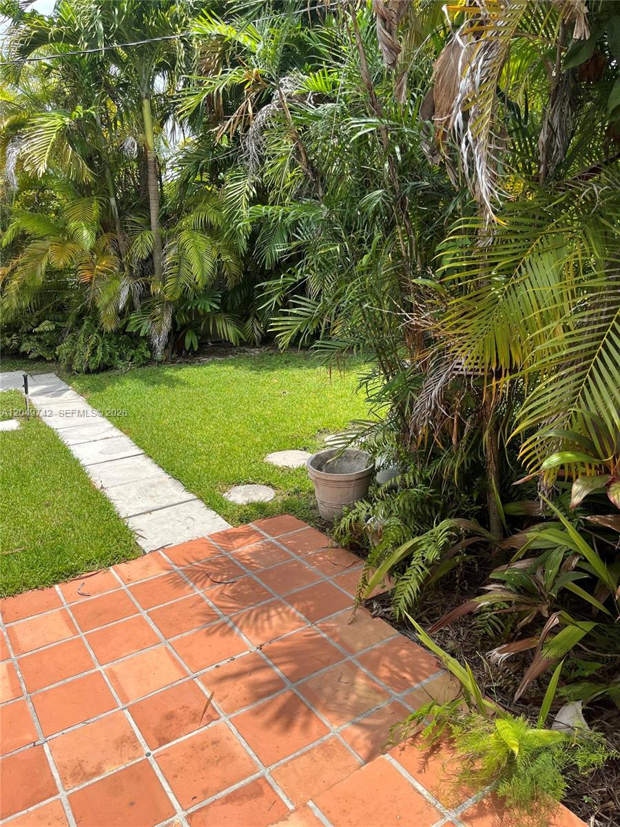A tiled patio leads to a grassy backyard surrounded by lush tropical palm trees — 5831 SW 89th Ct, Miami FL 33173, MIAMI, FL