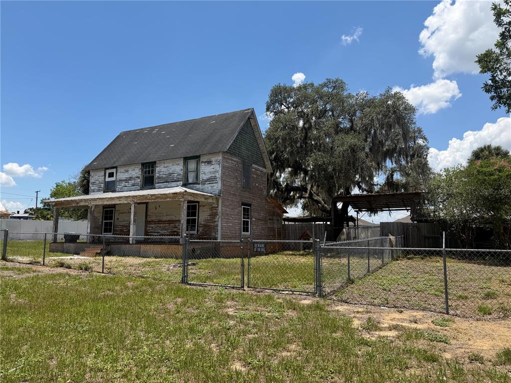 A weathered two-story house with a front porch stands behind a chain-link fence — 6115 COUNTY ROAD N, DAVENPORT, FL