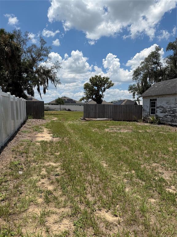 A grassy backyard features a white vinyl fence, a wooden fence, and an old shed — 6115 COUNTY ROAD N, DAVENPORT, FL