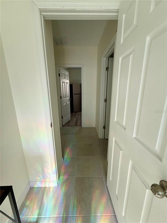 A hallway with light-colored tile flooring leads to a doorway showing a refrigerator — 1478 SEA GLASS ROAD, HAINES CITY, FL