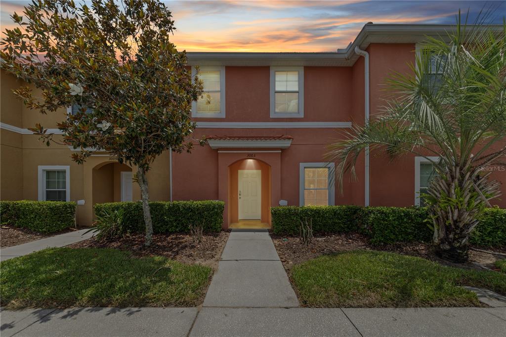 A two-story townhouse with a terracotta-colored exterior, a central front door, and manicured landscaping — 3003 BIRD OF PARADISE LANE, KISSIMMEE, FL