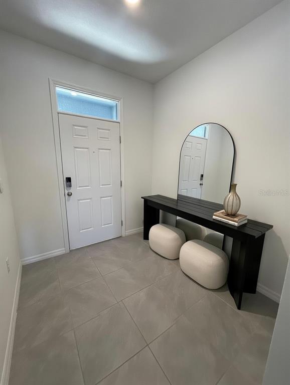 An entryway features a white door, a black console table, a mirror, and two ottomans — 32599 TURTLE GRACE LOOP, WESLEY CHAPEL, FL