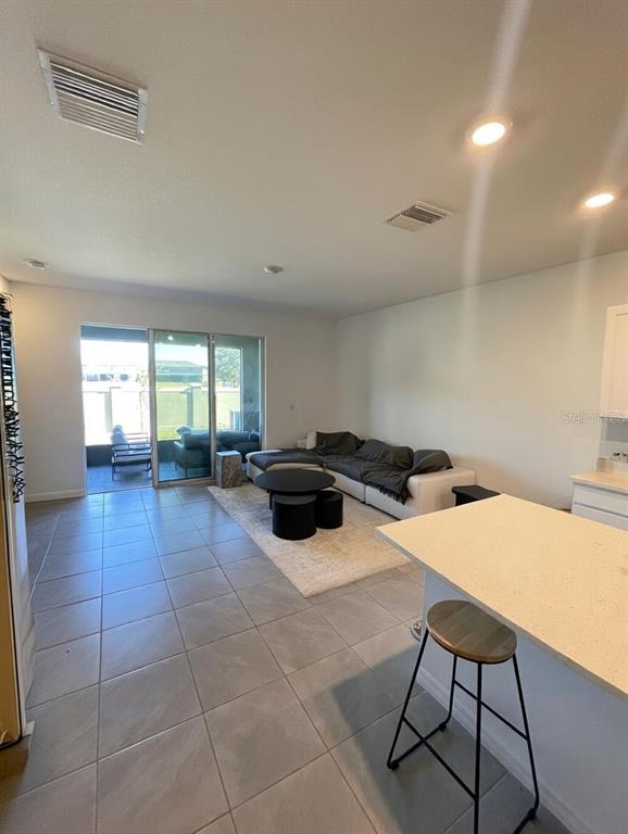 An open-concept living room features tile flooring, a sectional sofa, and sliding glass patio doors — 32599 TURTLE GRACE LOOP, WESLEY CHAPEL, FL