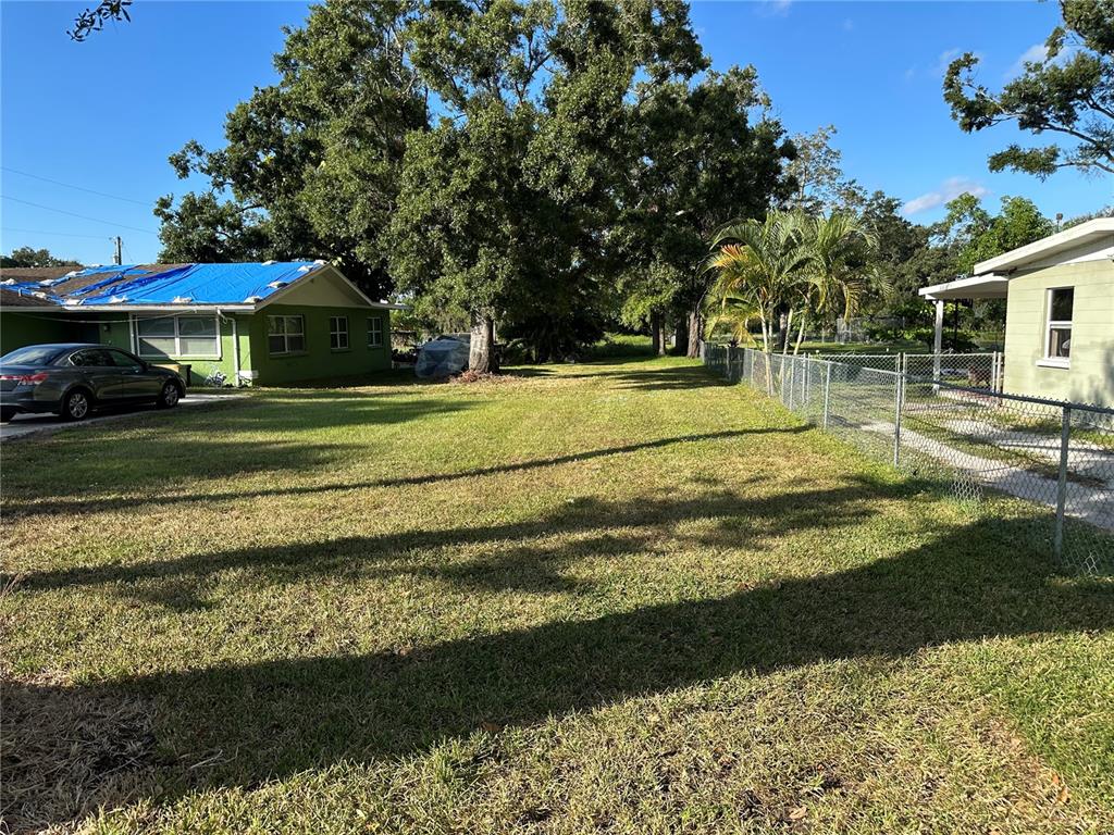 A grassy yard sits between a green house with a blue tarp and a fence — 302 12TH STREET W, PALMETTO, FL