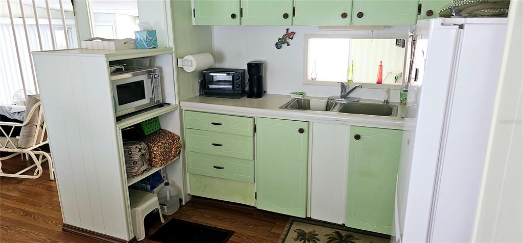 A small kitchen features light green cabinets, a microwave, a sink, and a white refrigerator — 10315 CORTEZ ROAD W UNIT 28-1, BRADENTON, FL
