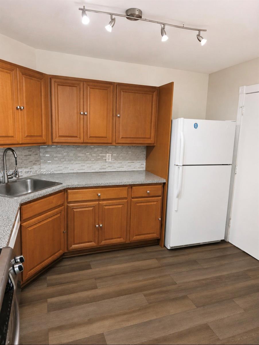 A kitchen features wood cabinets, granite countertops, a white refrigerator, and a track lighting fixture — LAUDERHILL, FL