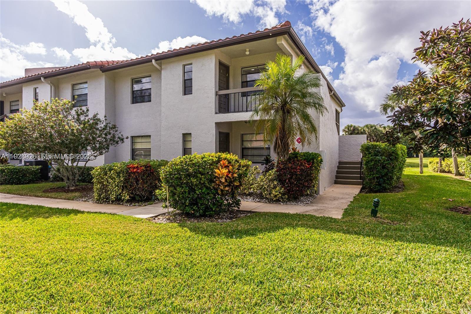A two-story stucco apartment building features a palm tree, landscaping, and a concrete walkway — 21529 Cypress Hammock Dr # 35J, Boca Raton FL 33428, BOCA RATON, FL
