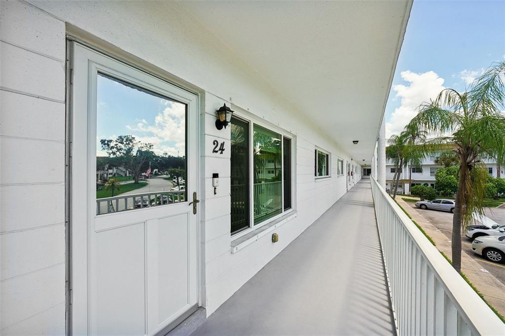 An exterior walkway leads to the entrance of a white apartment unit numbered 24 — 2430 BRAZILIA DRIVE UNIT 24, CLEARWATER, FL