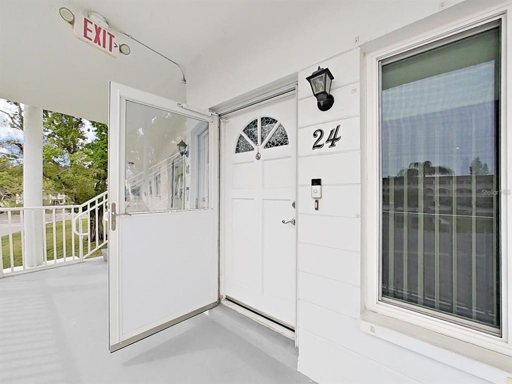 A white front door with a storm door is labeled with the number 24 — 2430 BRAZILIA DRIVE UNIT 24, CLEARWATER, FL