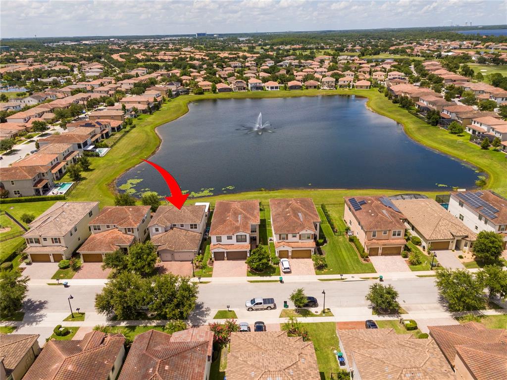 An aerial view shows a row of suburban houses facing a lake with a fountain — 10431 SIDDINGTON DRIVE, ORLANDO, FL