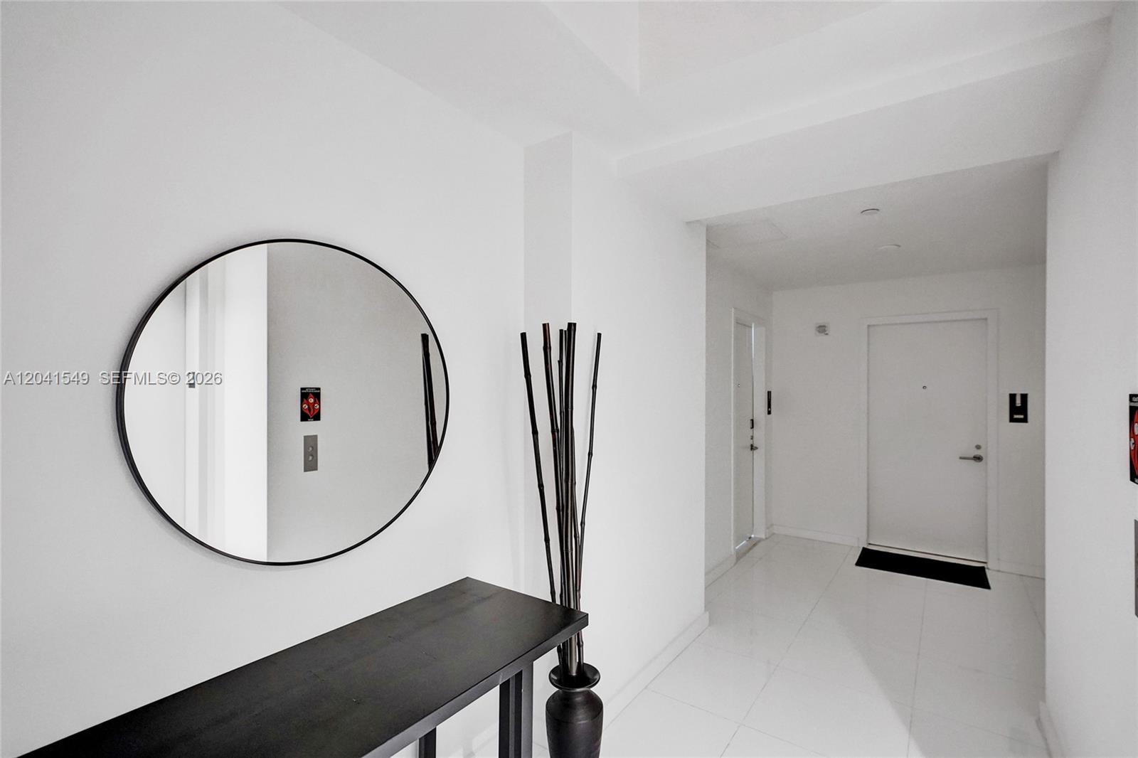 A minimalist white hallway features a round black-framed mirror, a black console table, and decor — 851 NE 1st Ave # 3800, Miami FL 33132, MIAMI, FL