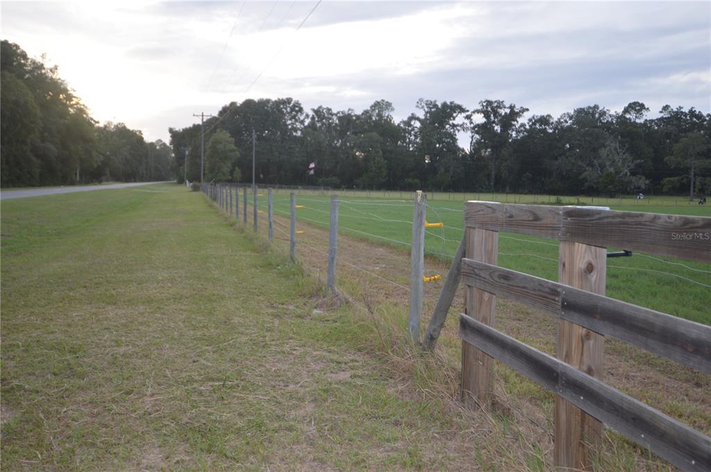 A wooden fence borders a grassy field alongside a road under a cloudy sky — 5640 SW COUNTY ROAD 344, TRENTON, FL