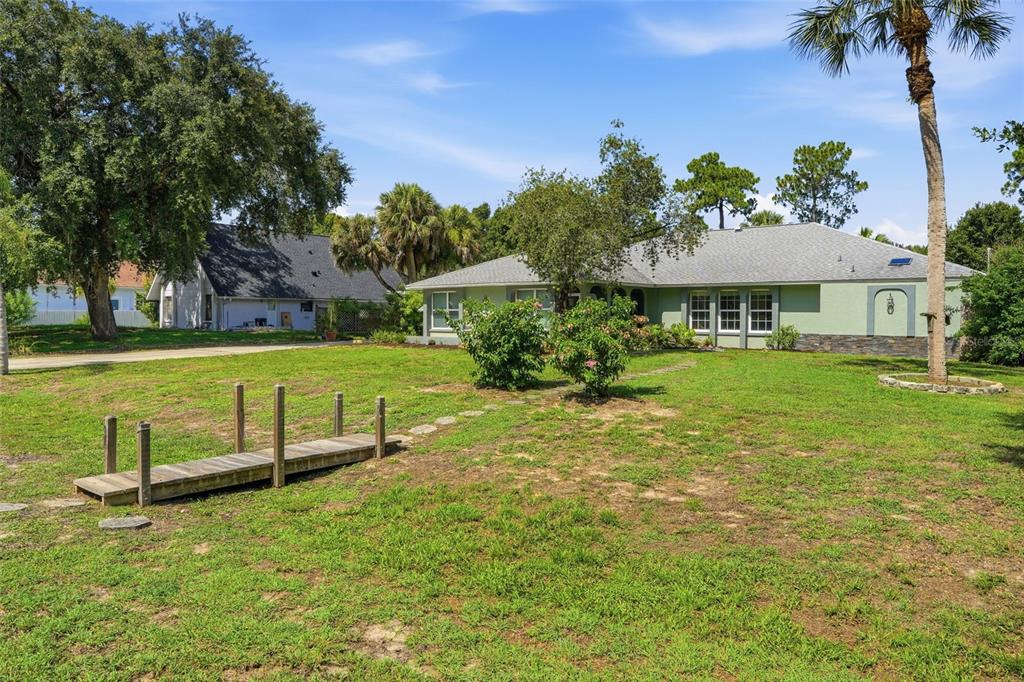 A single-story house with a green exterior, a wooden footbridge, and a palm tree — 505 THOMPSON AVENUE, LEHIGH ACRES, FL