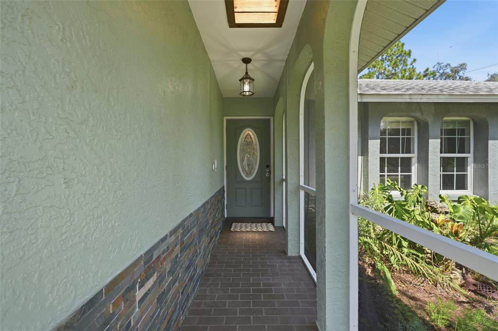 A covered entryway features a brick floor, stone wainscoting, and a green front door — 505 THOMPSON AVENUE, LEHIGH ACRES, FL