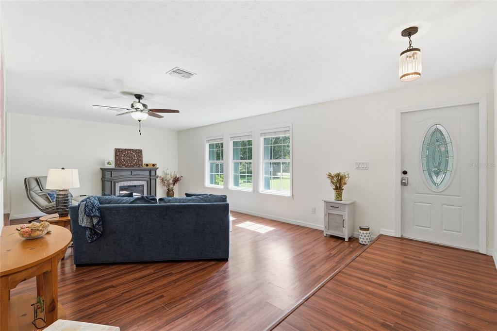 A living room with wood-look flooring, a blue sofa, a ceiling fan, and an entryway door — 505 THOMPSON AVENUE, LEHIGH ACRES, FL