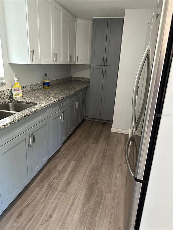 A kitchen features white upper cabinets, gray lower cabinets, granite countertops, and wood-look flooring — 108 EDGEWATER DRIVE, WINTER HAVEN, FL