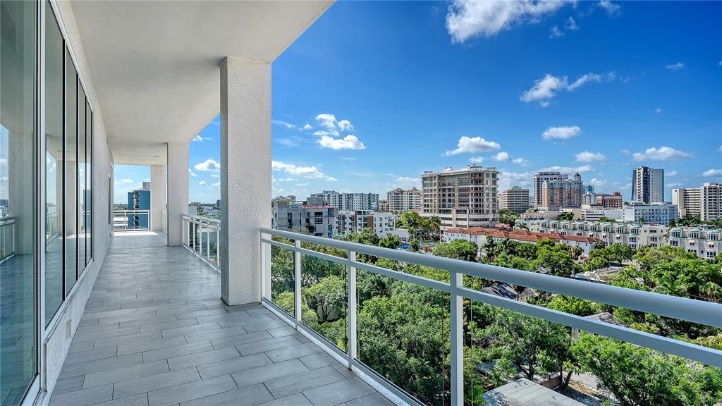 A spacious balcony with gray tile flooring and a glass railing overlooks a city skyline — 540 N TAMIAMI TRAIL UNIT 804, SARASOTA, FL