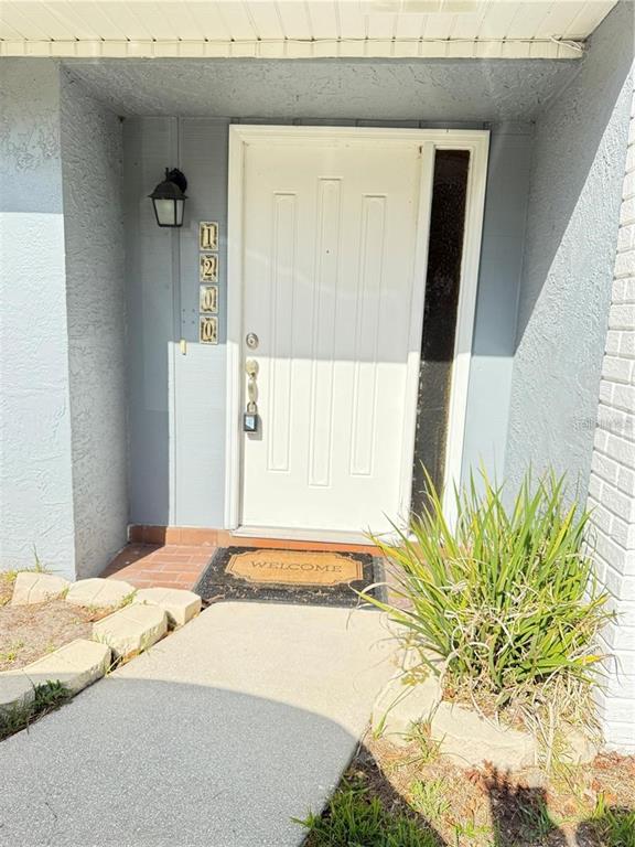 A white front door with a side light and house numbers sits under a porch — 1200 ABBEY CRESCENT LANE, CLEARWATER, FL
