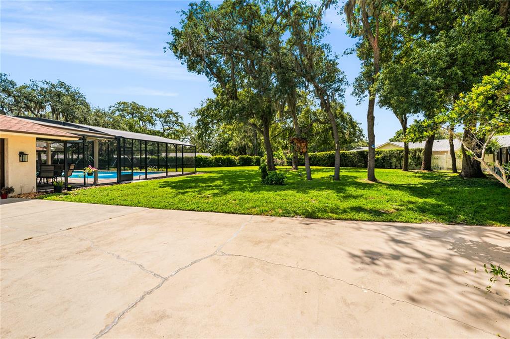 A concrete patio overlooks a large grassy backyard with mature trees and a screened pool — 111 LITTLE OAK LANE, ALTAMONTE SPRINGS, FL