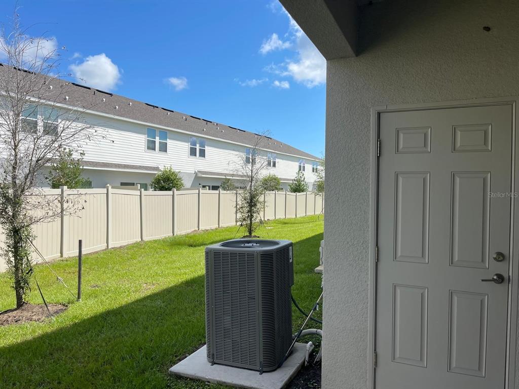 A backyard view featuring a tan vinyl fence, an HVAC unit, and a white door — 3335 COMPOSITION STREET, POINCIANA, FL