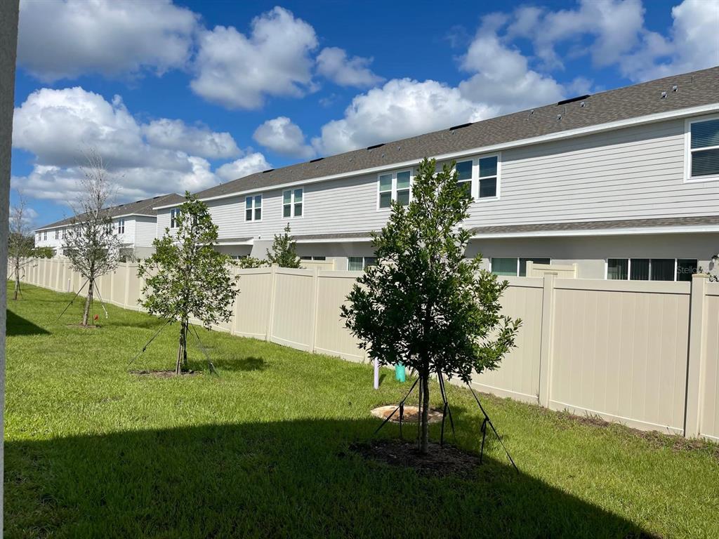 A backyard with a tan vinyl fence, young trees, and a two-story townhouse exterior — 3335 COMPOSITION STREET, POINCIANA, FL