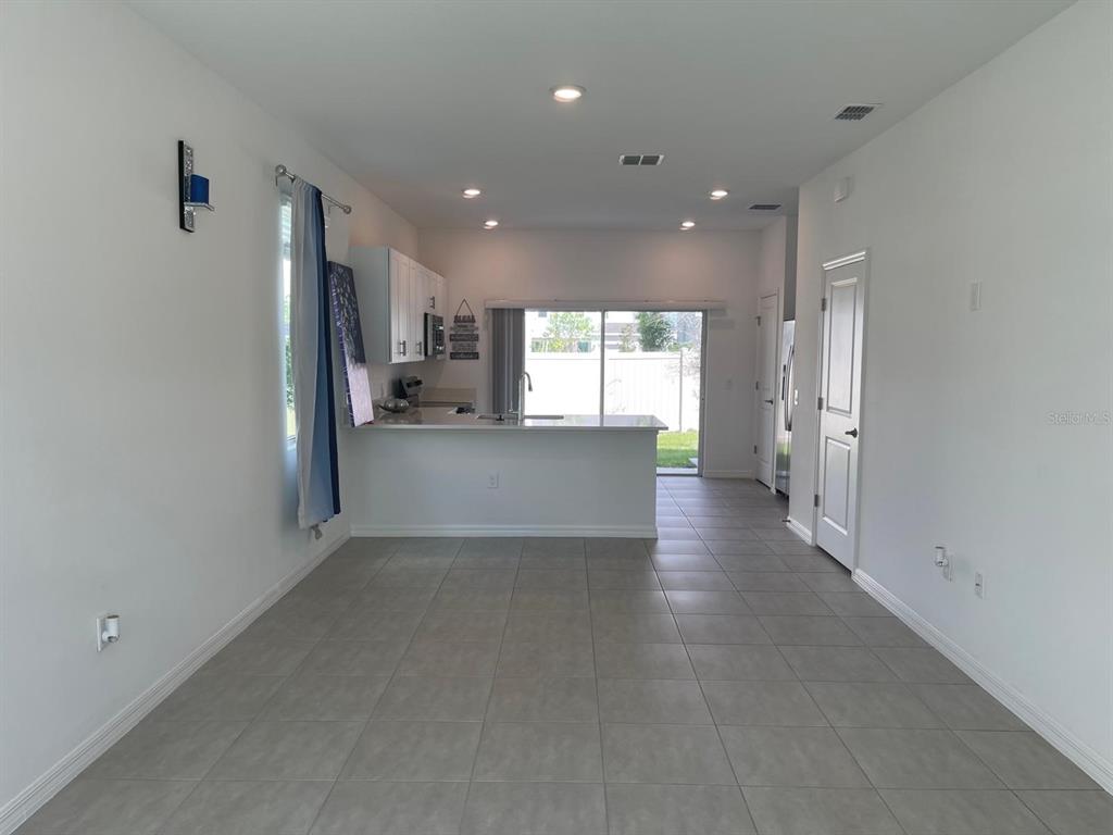 A kitchen with white cabinets and a breakfast bar overlooks a tiled living area — 3335 COMPOSITION STREET, POINCIANA, FL