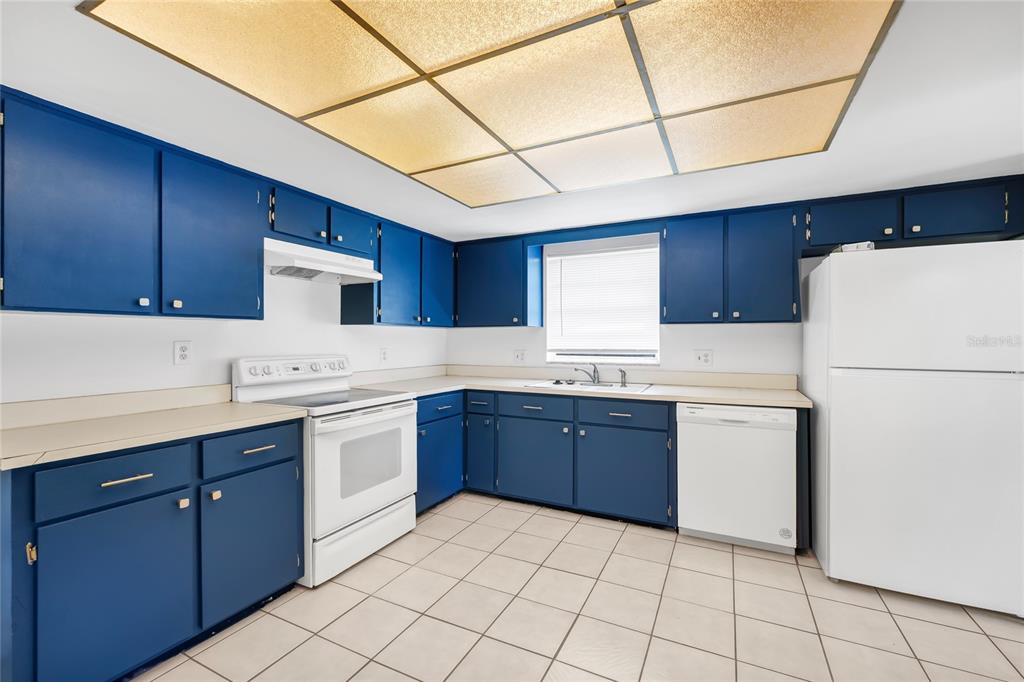 A kitchen features blue cabinets, white appliances, beige countertops, and a large grid ceiling light — 5060 ANDREA BOULEVARD, ORLANDO, FL