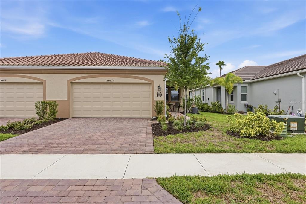 A beige single-story house with a two-car garage and a paved driveway — 20411 SYMPHONY PLACE, VENICE, FL