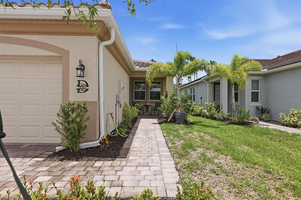 A paved walkway leads to the entrance of a beige house with a garage — 20411 SYMPHONY PLACE, VENICE, FL