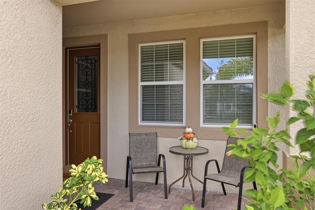 A covered front porch features two chairs, a small table, and a brown front door — 20411 SYMPHONY PLACE, VENICE, FL