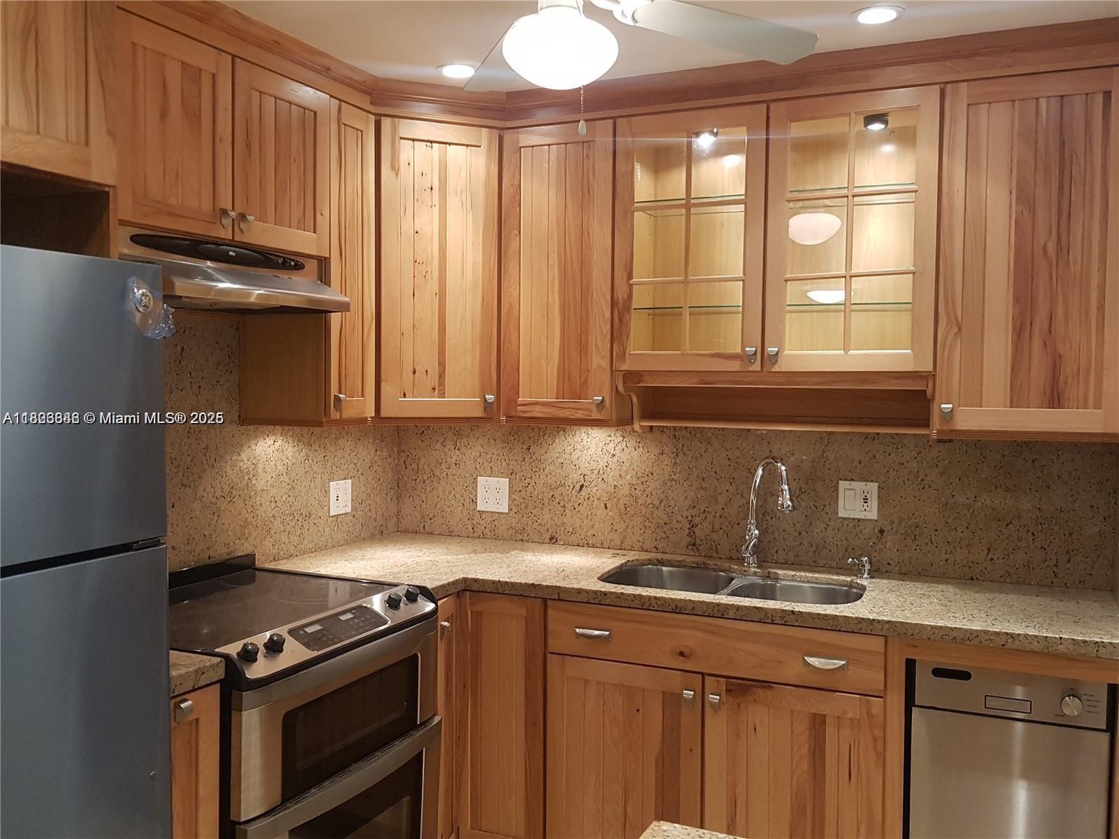 A kitchen features natural wood cabinets, granite countertops, stainless steel appliances, and under-cabinet lighting — 253 S Cypress Rd # 237, Pompano Beach FL 33060, POMPANO BEACH, FL